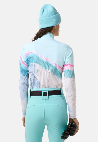 A long-sleeve, light blue top with mountain graphic patterns in white, pink, and darker blue. Paired with mint green pants, holding black gloves.