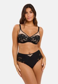 Ensemble de lingerie noire comprenant un soutien-gorge en dentelle festonnée avec des panneaux en mesh et des culottes taille haute. Motif floral délicat et accents de nœud subtils.