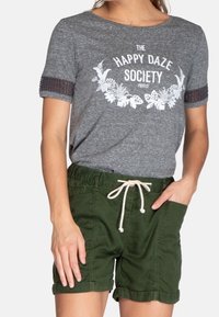 Camiseta gris con estampado floral blanco y mangas cortas, combinada con pantalones cortos verdes con cintura ajustable y dobladillos enrollados.
