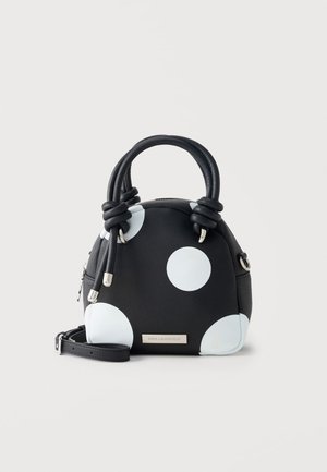 Black handbag with large white polka dots, two knotted handles, silver zipper and detachable shoulder strap, set against plain background.