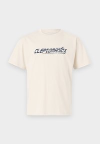 Cream-colored cotton t-shirt with short sleeves featuring bold blue text "CLEPTOMANICX" across the front. Simple crew neckline and relaxed fit.