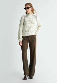 Maglione spesso di colore crema con un motivo testurizzato, abbinato a jeans marroni a gamba dritta e stivaletti con tacco a punta di colore marrone.