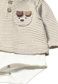 Pijama para bebé a rayas beige y blancas con botones cerca del cuello y un pequeño bolsillo con la cara de un perro adorable y orejas de tela.