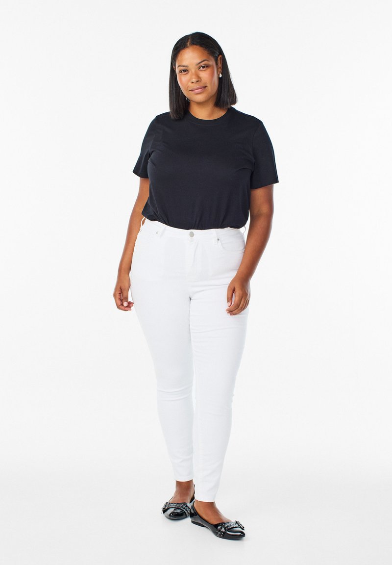 Camiseta negra de manga corta combinada con jeans ajustados blancos. El modelo lleva zapatos planos negros con detalle de lazo. Diseño de atuendo simple y clásico.