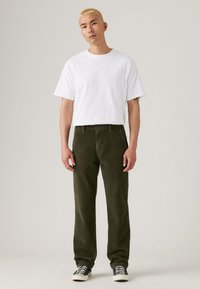 Weißes T-Shirt mit kurzen Ärmeln, kombiniert mit dunkelgrünen Cordhosen. Die Hosen haben eine gerade Passform, sichtbare Nähte und Seitentaschen. Schwarz-weiße Sneakers.