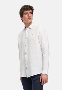 Witte linnen blouse met lange mouwen en een button-down kraag, voorzien van houten knopen en een klein geborduurd logo op de borst.