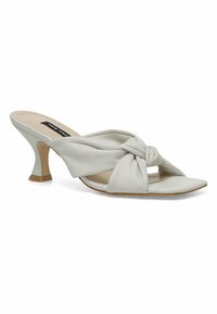 Mules in soft white leather featuring a knotted design and open toe. Structured heel with a square base, pointed toe shape, and smooth texture.