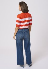 Red and white striped knit shirt with short sleeves paired with high-waisted, wide-leg blue denim jeans.
