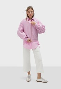 Roze bomber jakna na zatvaranje s balon rukavima preko svijetlo ružičaste košulje, uparena s bijelim širokim hlačama i bijelim tenisicama s detaljima.