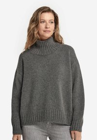 Grauer gestrickter Pullover mit hohem ribbeligem Rollkragen, fallenden Schultern und ribbeligem Saum. Die Textur ist weich und grob, ideal zum Schichten.