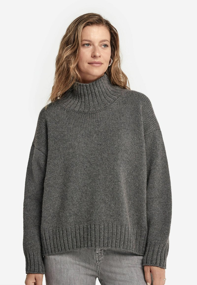 Grauer gestrickter Pullover mit hohem ribbeligem Rollkragen, fallenden Schultern und ribbeligem Saum. Die Textur ist weich und grob, ideal zum Schichten.