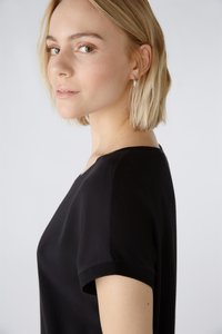 Schwarzes Kurzarmoberteil mit rundem Ausschnitt, glatter Textur und nahtlosem Design, seitlich betrachtet und minimalistischen Stil zeigend.