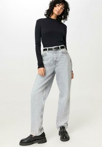 Schwarzes Langarmoberteil, hellgraue weite Jeans mit hoher Taille, schwarzer Gürtel und klobige schwarze Loafer mit Plateau-Sohle.