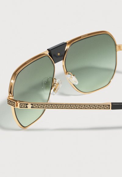 Γυαλιά ηλίου με χρυσό πλαίσιο και φακούς με πράσινο φίλτρο, μαύρη γέφυρα και βραχίονες με χρυσό σχέδιο ελληνικού κλειδιού και έμβλημα της Μέδουσας.