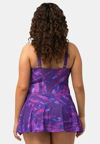 Robe de bain violette avec un motif floral dans des teintes de rose et de bleu. Elle dispose de bretelles réglables et d'un design évasé, fabriquée en matériau extensible.