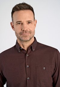 Camisa marrón con botones, tela texturizada, cuello abierto y un solo bolsillo en el pecho. Presenta botones en contraste en la tapeta y el bolsillo.