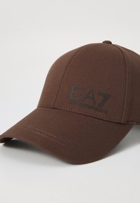 Smeđa bejzbol kapa napravljena od teksturirane tkanine. Ima zakrivljeni vizir i urezani crni logo "EA7" na prednjem panelu.