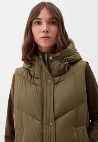 Olijfgroen gewatteerd vest met een capuchon, voorzien van een ritsluiting, trekkoorden en contrasterende bruine mouwen. Opvallende stiksels op de voorkant.