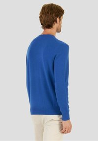 Blå stickad tröja med lång ärm, rund hals och ribbade muddar. Mjuk textur, figurnära passform, minimalistisk design och inga synliga mönster.