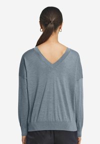 Jasnoniebieski sweter w serek z długimi rękawami i luźnym krojem, z prążkowanymi mankietami i dołem. Miękka, gładka tekstura.