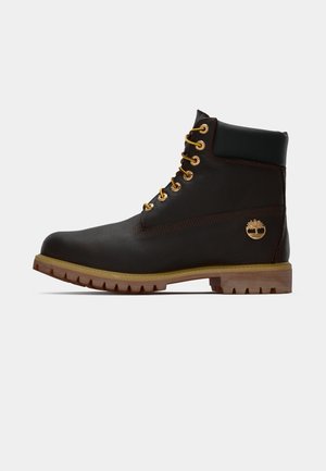 Sorte læder ankelstøvle med gyldne øjer, brune detaljer og gummisål. Har en polstret krave og præget logo på siden.