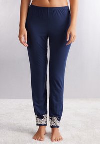 Marineblauwe lichtgewicht loungebroeken met een elastische tailleband en delicate witte laceaccenten aan de manchetten. Zachte, gladde textuur overal.