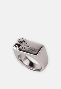 Bague en ton argentée présentant un design carré. Le dessus arbore des motifs de dés et le marquage gravé "Don Ed Hardy" sur le côté. Texture lisse.