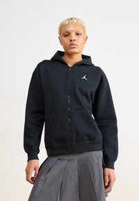 Sudadera con cremallera negra, hecha de un tejido suave, que cuenta con un bolsillo tipo canguro y un logo Jumpman blanco en el pecho. Tiene un corte ligeramente holgado.