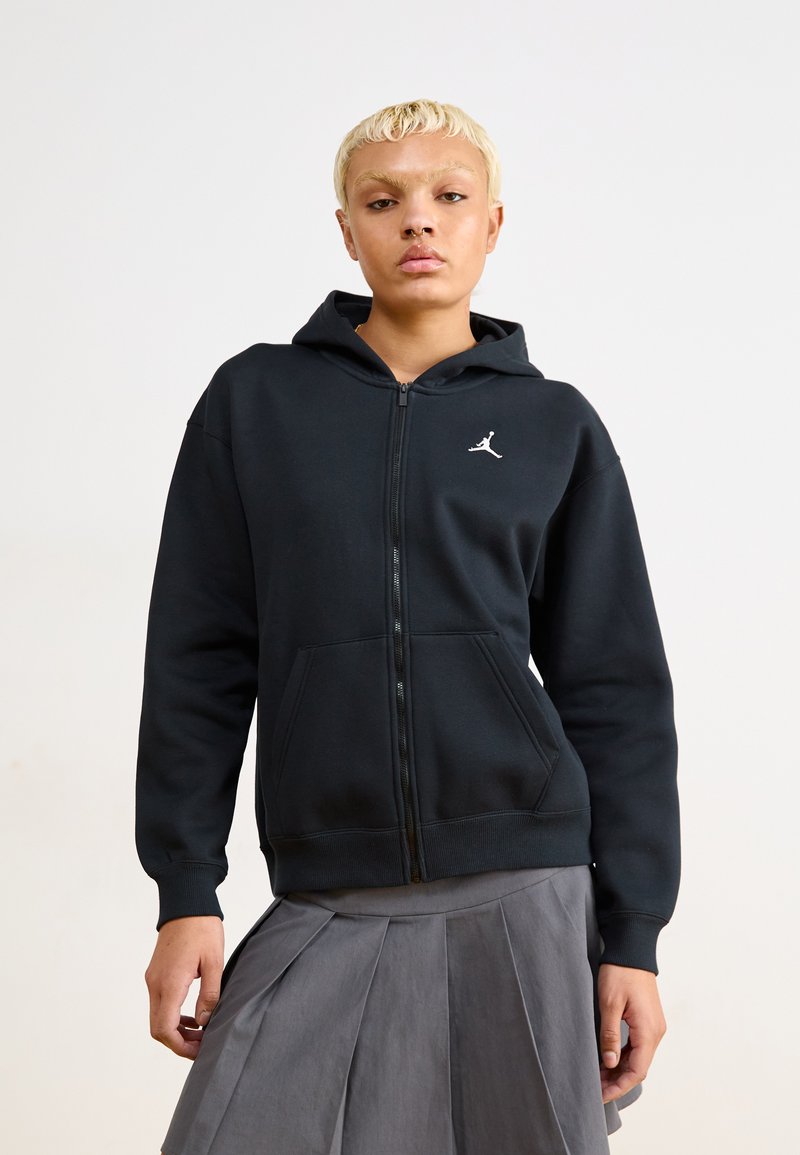 Sudadera con cremallera negra, hecha de un tejido suave, que cuenta con un bolsillo tipo canguro y un logo Jumpman blanco en el pecho. Tiene un corte ligeramente holgado.