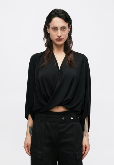 Black, loose-fitting top with a V-neck and draped design, paired with high-waisted black cargo pants featuring side pockets and snap accents.