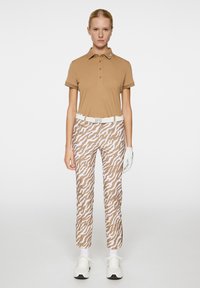 Brun polo skjorte med korte ermer, kombinert med bukser i hvite og brune zigzag-mønstre. Hvit belte og detalj med sneakers synlig.