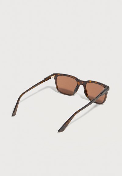 Lunettes de soleil carrées écaille de tortue avec des verres marron et des branches fines, présentées sur un fond clair uni.