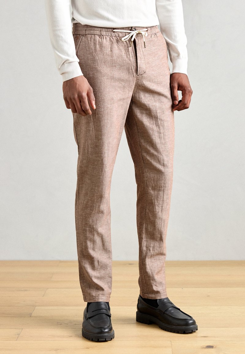 Pantalons en lin mélangé de couleur marron clair, avec une taille à cordon, des poches latérales et une coupe slim. Associés à des mocassins en cuir noir.