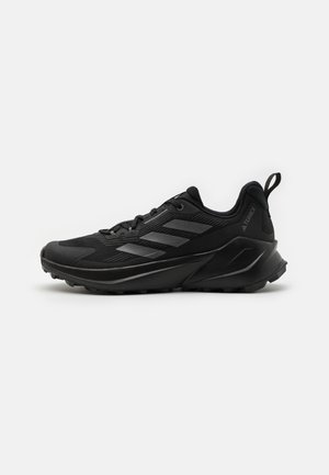 Czarne sportowe sneakersy z teksturowaną cholewką, czarną gumową podeszwą i odblaskowymi akcentami. Zaprojektowane do użytku na świeżym powietrzu z wytrzymałym profilem.