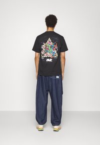 Černé grafické tričko s barevným designem Marvel na zadní straně, spárované s volnými tmavými džíny a vícebarevnými botami.