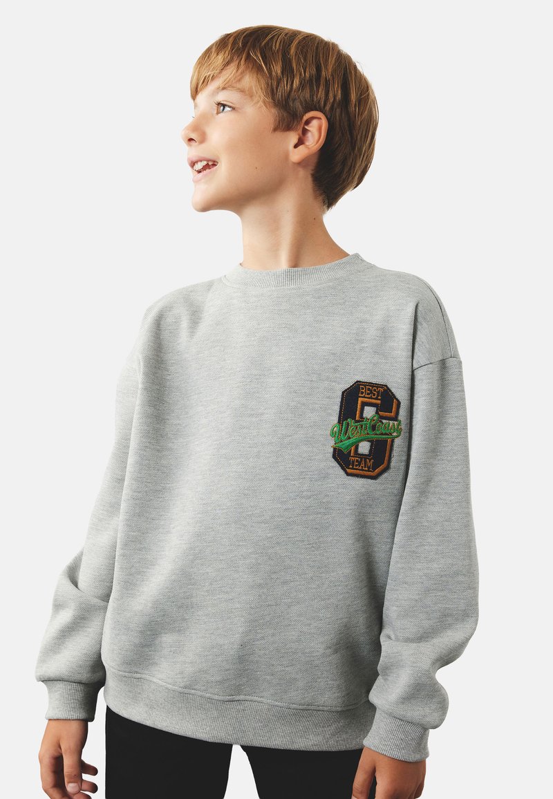 Grå sweatshirt med rund halsudskæring og lange ærmer. Har et farverigt broderet patch på venstre bryst med teksten "BEDSTE HOLD."