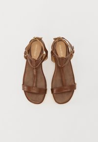 Brown leather sandals with two adjustable straps, a T-bar design, and a smooth texture, featuring a cushioned insole and flat sole.