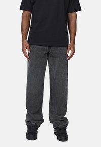 T-shirt nera a maniche corte abbinata a jeans in denim grigio scuro a vestibilità ampia, con design a gamba dritta e dettagli minimi.