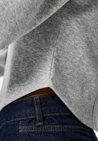 Sweat-shirt gris à texture douce, avec un ourlet inférieur arrondi. Porté avec un jean bleu foncé orné de détails de surpiqûres jaunes.