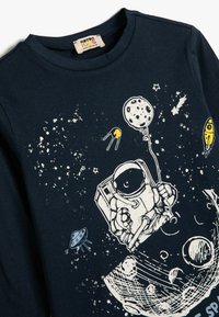 Granatowa bawełniana koszula z długim rękawem, z grafiką astronauty, planetami i statkami kosmicznymi w białym i żółtym kolorze z przodu.
