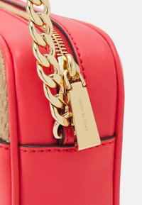 Červená kožená kabelka s pozlaceným řetízkem, zipovým uzavíráním a štítkem s vyrytým nápisem "MICHAEL KORS." Wzor na jedné straně.