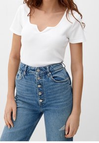 Vit ribbad kortärmad topp med V-ringning, kombinerad med högmidjade blå jeans i denim med fem-knapplås och slitningar.