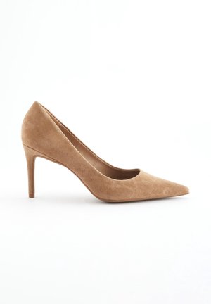 Escarpin à talon haut en daim beige, bout pointu, avec un talon aiguille fin, présenté sur un fond blanc.