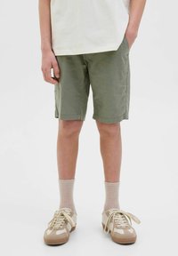 Olivgröna shorts med sidofickor, kombinerat med ljuscremefärgade ribbade strumpor och beige sneakers med en mix av texturer och snörningar.