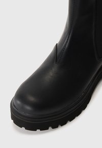 Must musta kärgstringidega nahast ankle saapad, millel on ümar nina, elastsed külg-paneelid ja tekstureeritud kummist tald, mis on varustatud sügavate soontega haardumise tagamiseks.