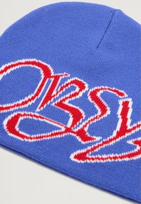 Gorro de punto azul con una textura suave que presenta un destacado diseño de logotipo rojo y blanco. El sombrero tiene una forma redondeada y detalles de costura mínimos.