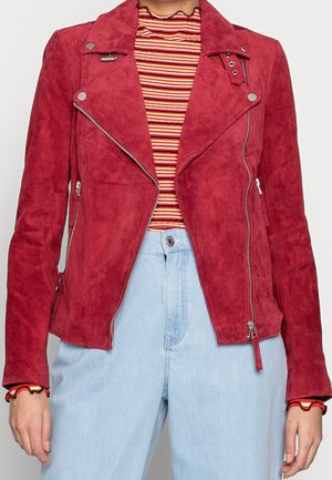 Person iført en rød ruskind bikerjakke over en rød, orange og hvid stribet top, kombineret med lyseblå højtaljede jeans.