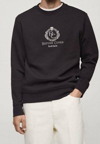 Sudadera negra hecha de una mezcla de algodón, con un logo y el texto "Refuge Cover Book Oasis" en blanco, puños y dobladillo acanalados.