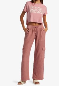 Różowy krótki t-shirt z białym nadrukiem tekstowym; zestawiony z różowymi szerokimi spodniami o fakturze, posiadającymi boczne kieszenie i ściągacz w pasie.