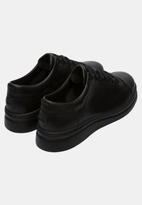 Black leather sneakers featuring a smooth finish, round toe, flat laces, and thick rubber sole with minimal stitching and logo detail.